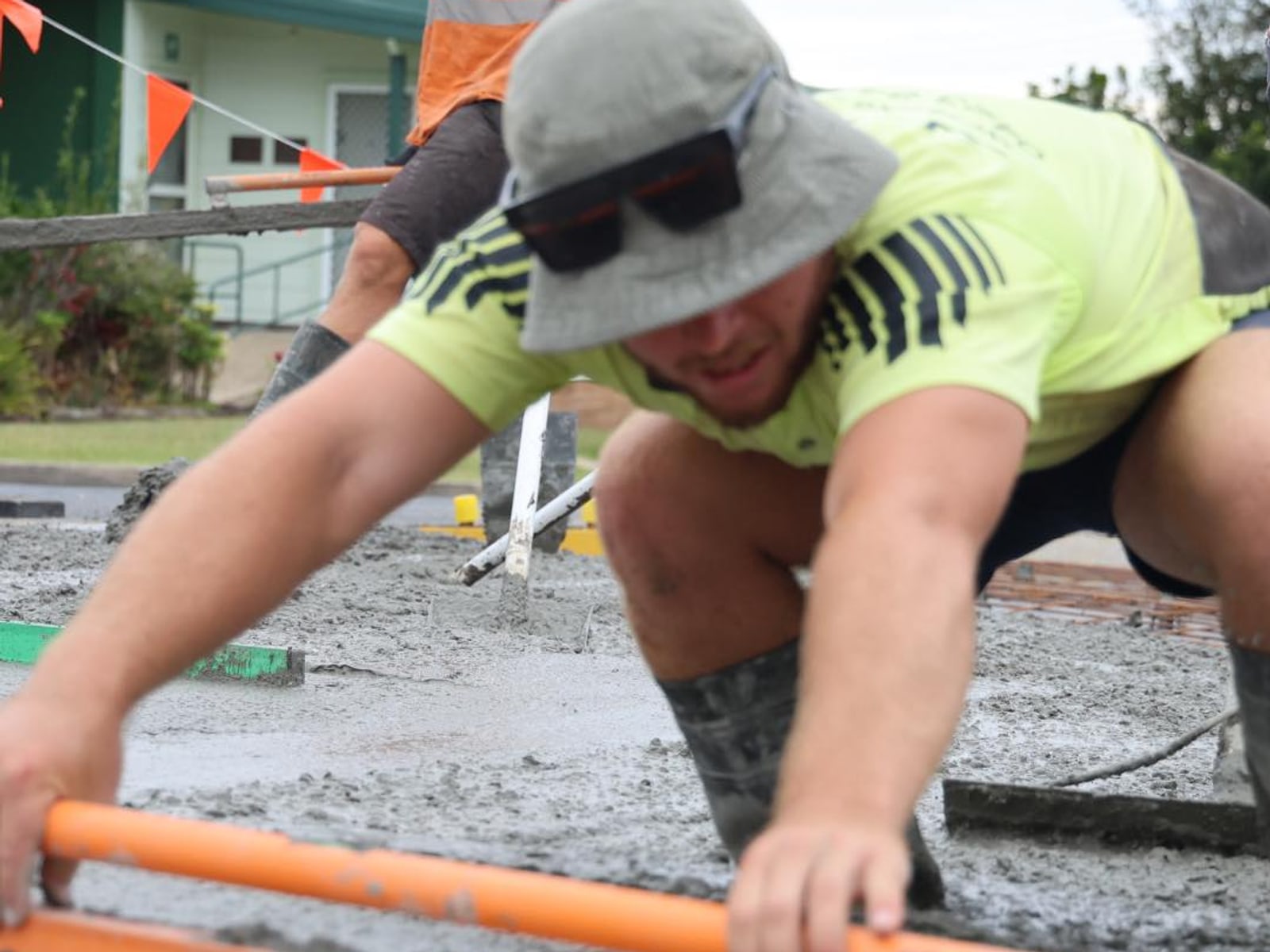 Boots and shovel mid-pour in fresh wet concrete — the screed in motion